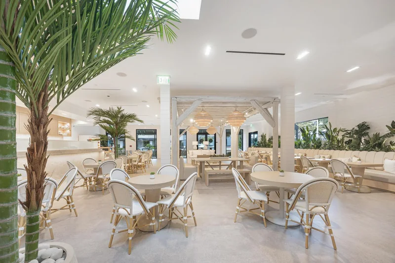 The Pura Vida dining room, a bright white space with rattan chairs, timber beams and interior palms