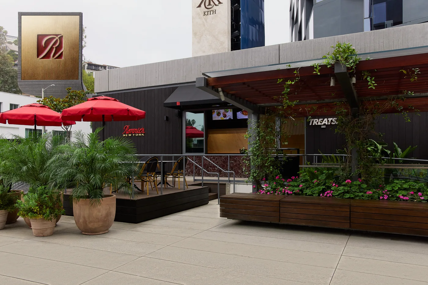 The Kith Treats café terrace at KITH West Hollywood, red umbrellas above planted beds
